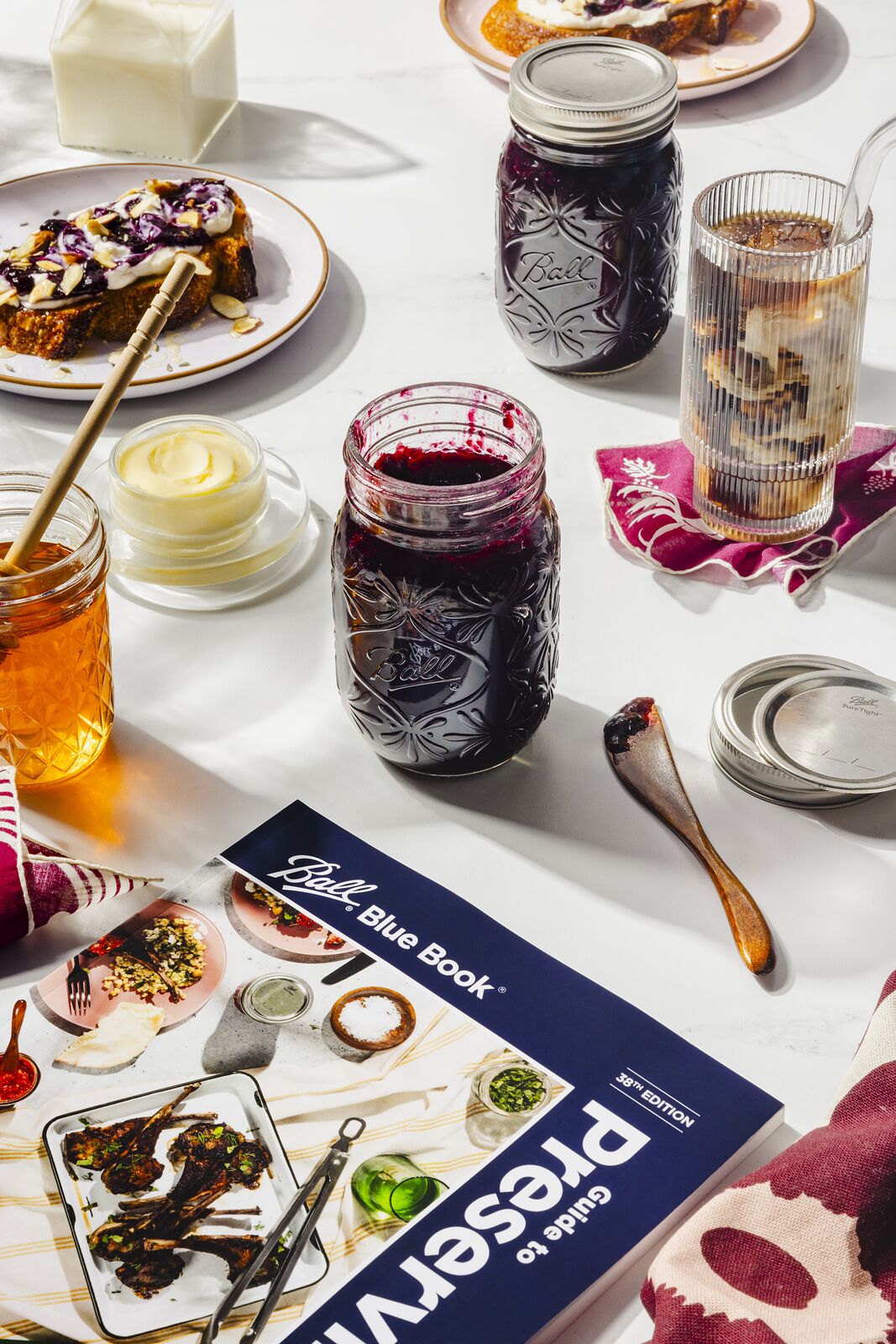 The same brunch table with the Ball Blue Book Guide to Preserving laid open beside the jars