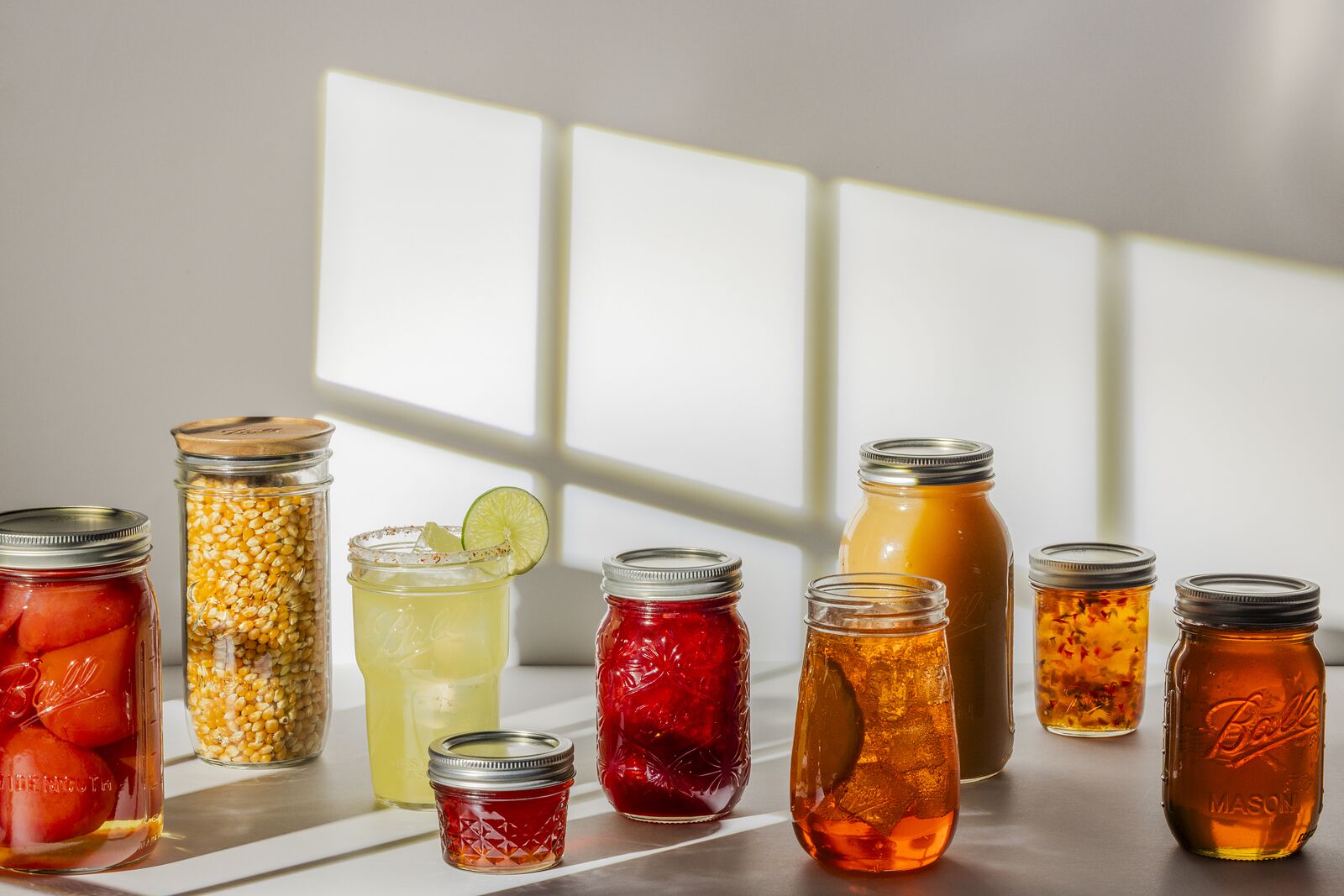 Shelf of home-canned tomatoes, corn, peppers and peaches in Ball jars, backlit by a window