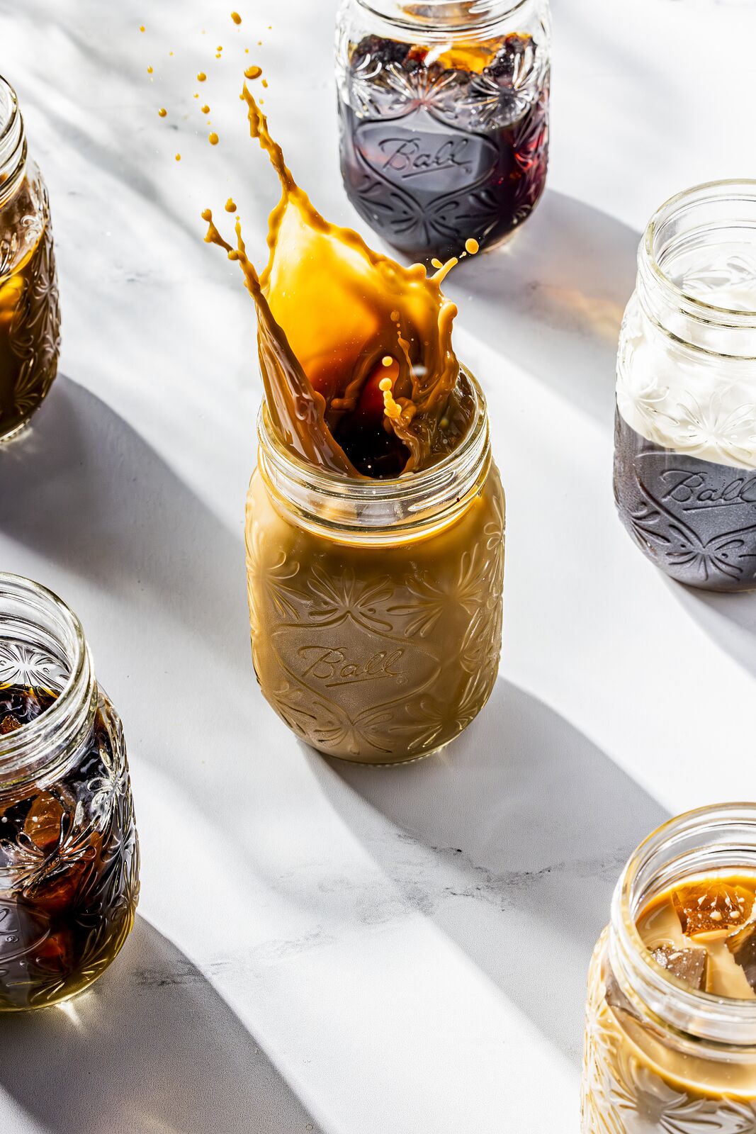 Coffee poured into a Ball jar from above, jars of dark preserves alongside
