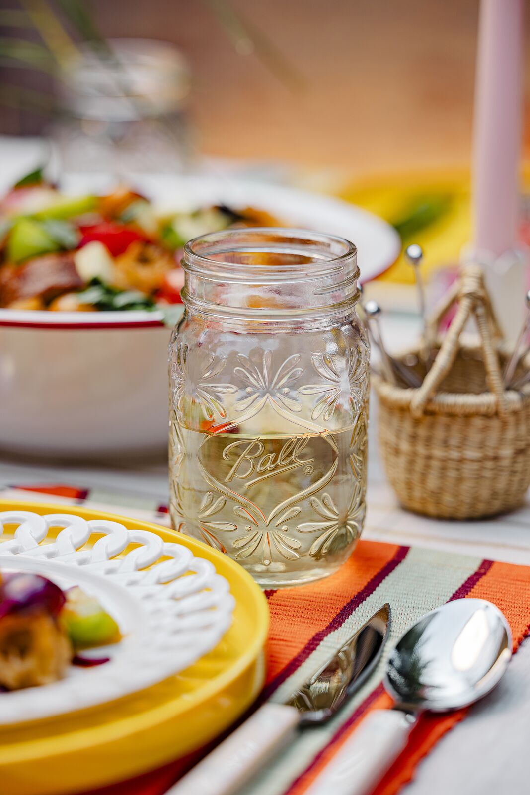 Outdoor place setting at golden hour with a Ball jar drink beside a yellow plate