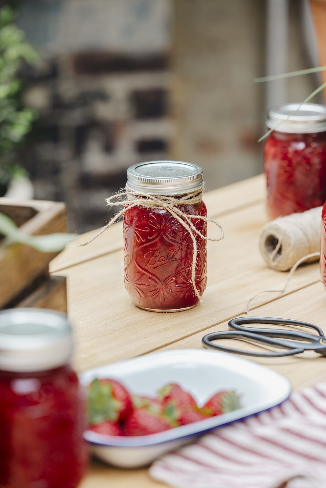 Sealed jar of red jam finished with a twine tie on a wooden work table
