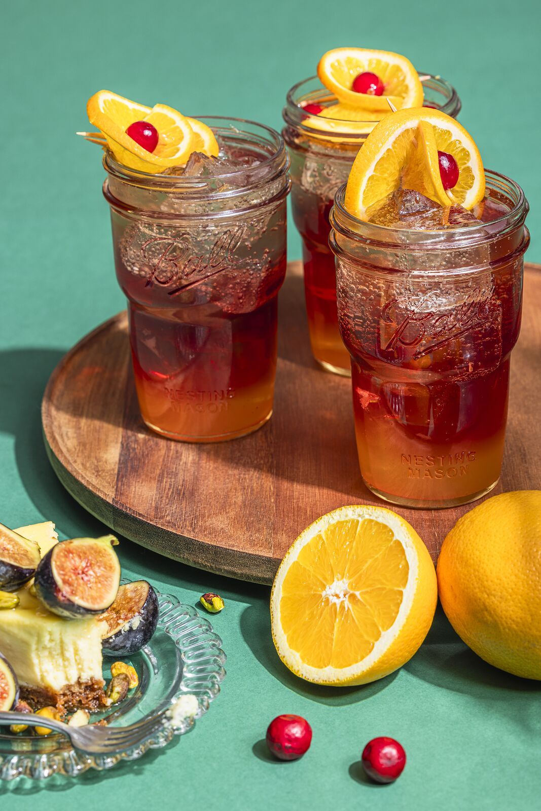 Two Ball jar drinks with orange twists on a round wooden board against teal