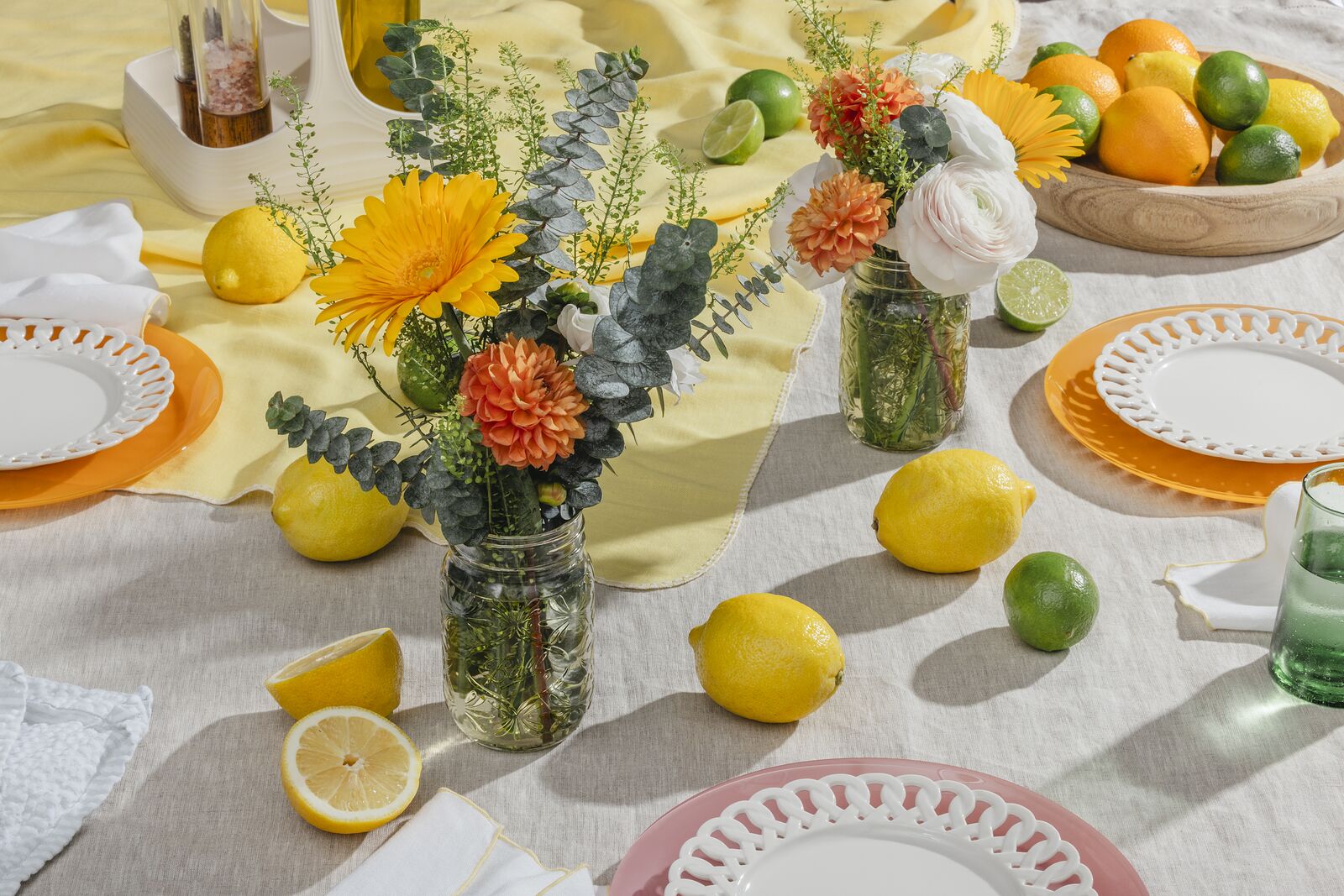 Outdoor table set with flowers arranged in a Ball jar, lemons and limes across the cloth