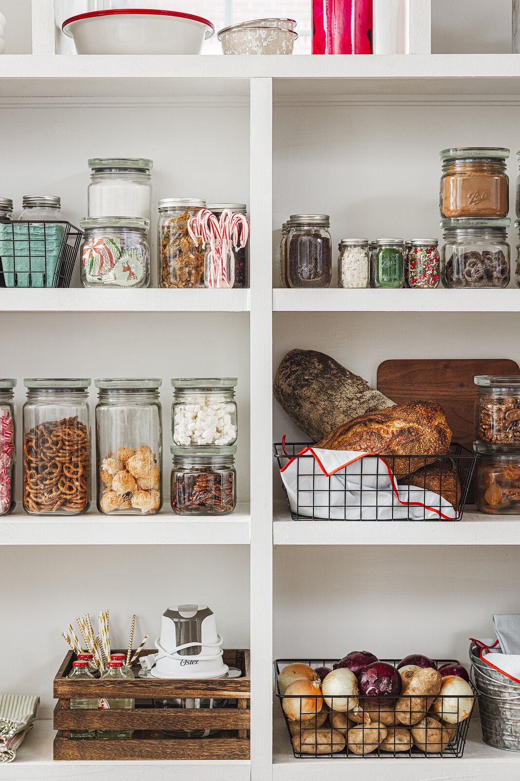Pantry shelving holding jars of dry goods, a loaf of bread and baskets of onions and garlic