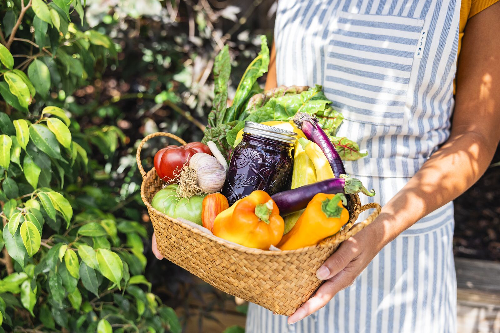 Gift basket of garden produce and a jar of preserves held against dense green foliage