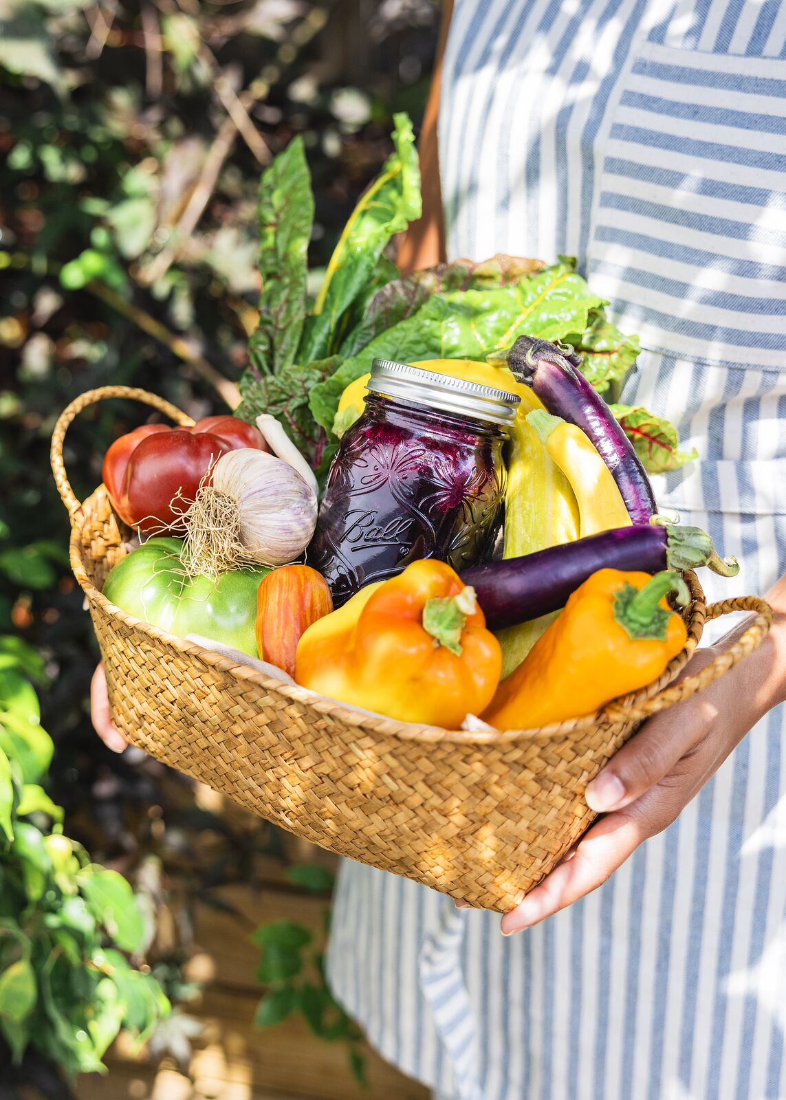 Basket of peppers, eggplant, chard and garlic carried with a sealed Ball jar of dark preserves tucked inside